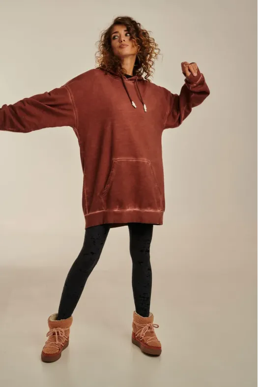 Person wearing a long rust-colored hoodie with black leggings and brown boots on a plain background