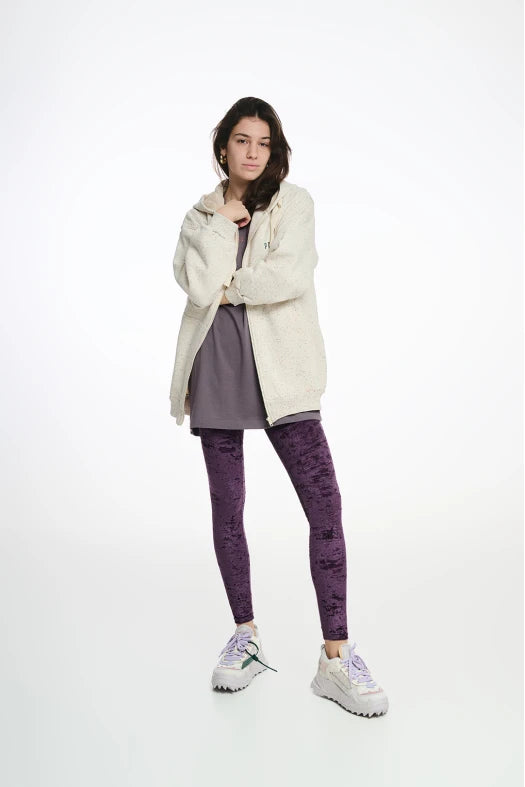 Person wearing a cream jacket, gray dress, purple leggings, and white sneakers on a white background