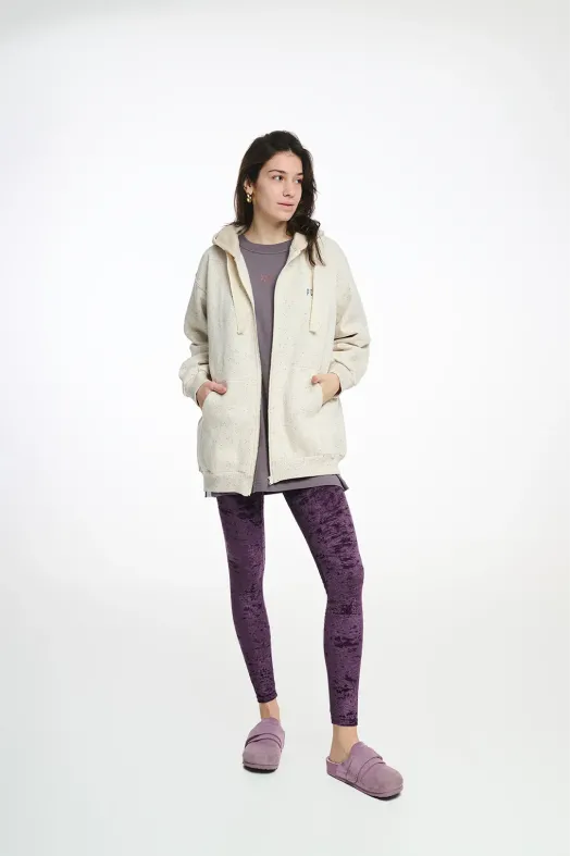 Woman wearing a cream hoodie and purple leggings on a white background