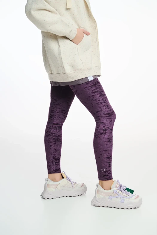 Person wearing a cream coat, purple leggings, and white sneakers on a white background