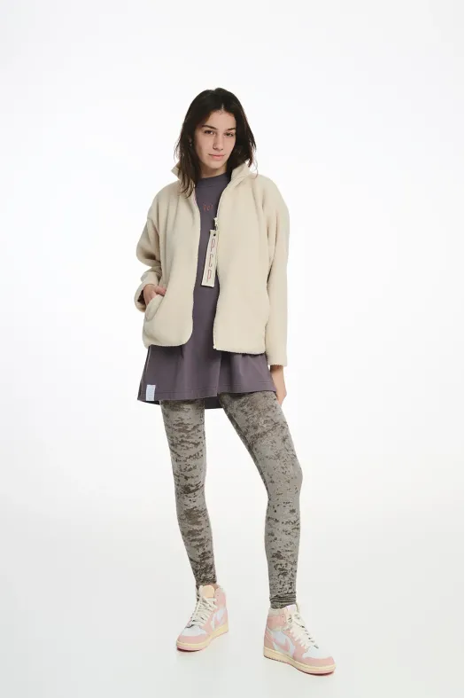 Woman wearing a beige jacket, purple dress, and patterned leggings on a white background