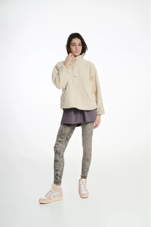 Person wearing a beige jacket, gray leggings, and white sneakers on a white background