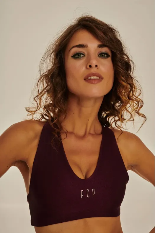 Woman wearing a dark purple sports bra with 'PCP' branding against a neutral background