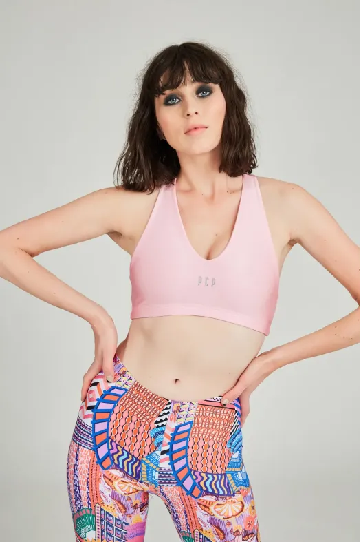 Woman wearing a pink sports bra and colorful patterned leggings on a plain background