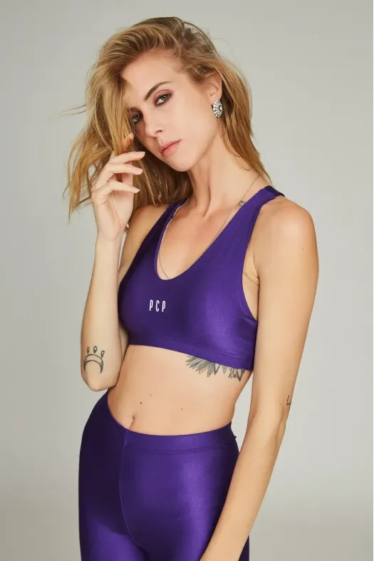 Woman wearing a purple sports bra and leggings against a gray background