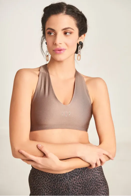 Woman wearing a brown sports bra with a brand logo on a plain background
