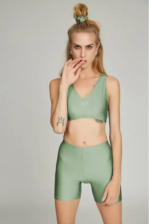 Woman wearing a green sports bra and shorts set on a plain background
