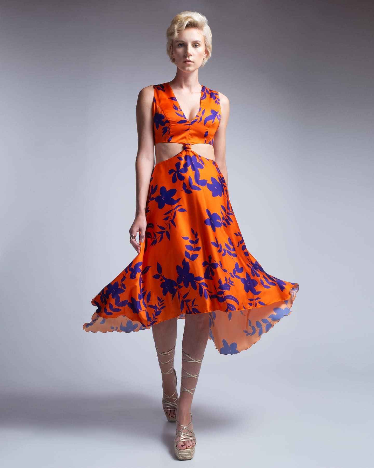 Woman wearing an orange dress with blue floral pattern on a gray background