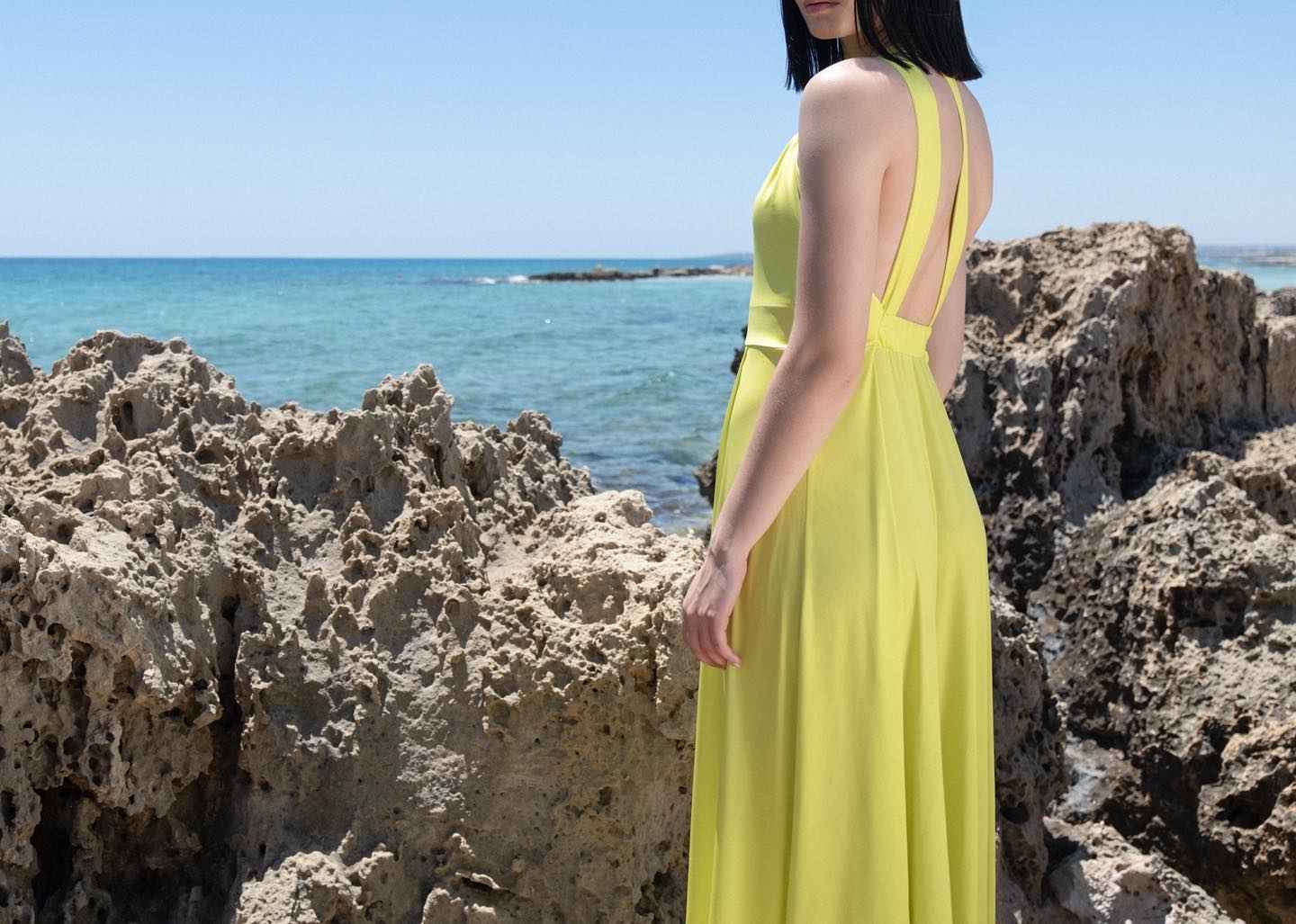Woman in a yellow dress standing on rocky beach with ocean in the background
