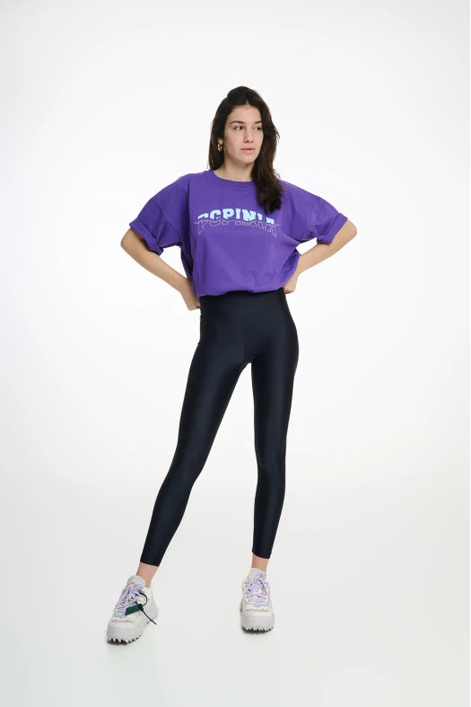 Person wearing a purple oversized t-shirt and black leggings on a white background