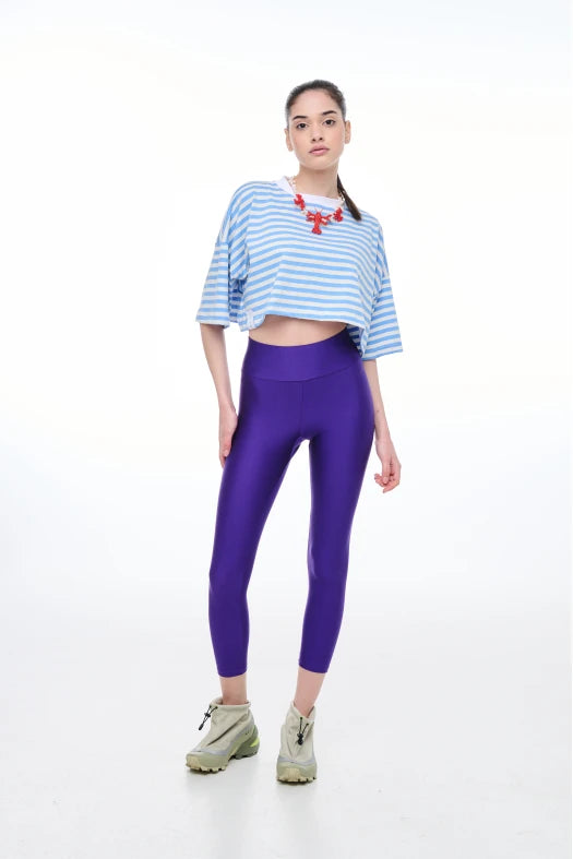 Woman wearing a blue and white striped crop top and purple leggings on a white background