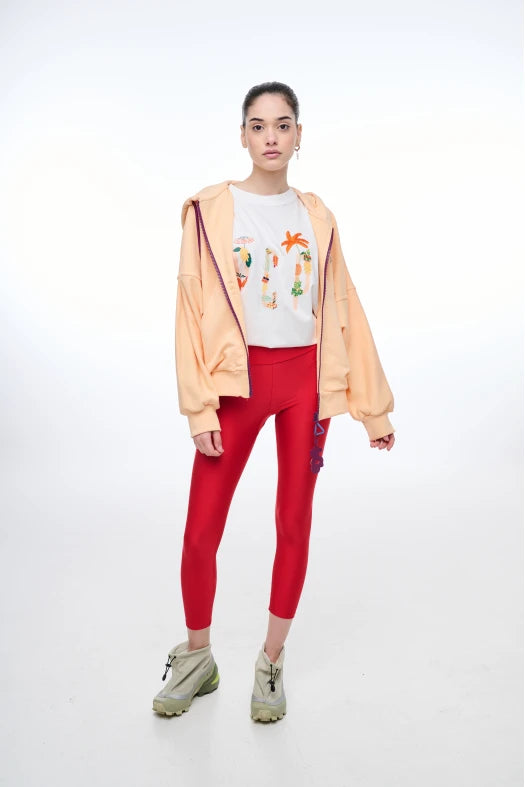 Person wearing a peach jacket, white t-shirt with graphics, red leggings, and beige boots on a white background