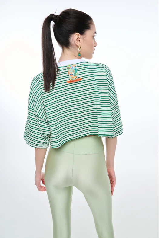 Woman wearing a green and white striped shirt with a graphic on the back, standing against a white background.