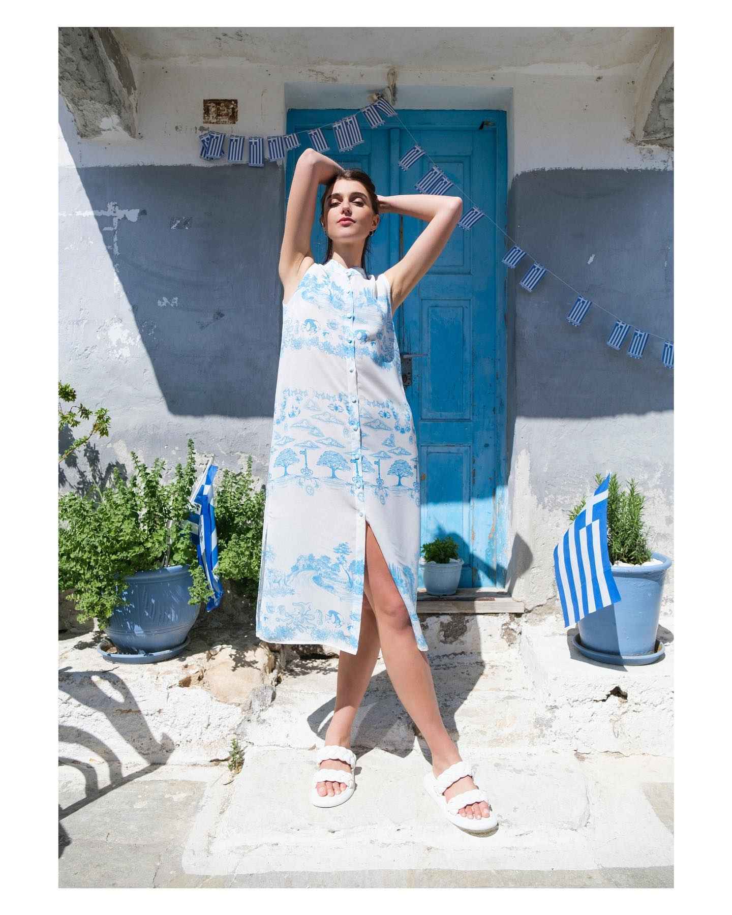 Woman in a blue and white dress standing in front of a blue door with Greek flag decorations.
