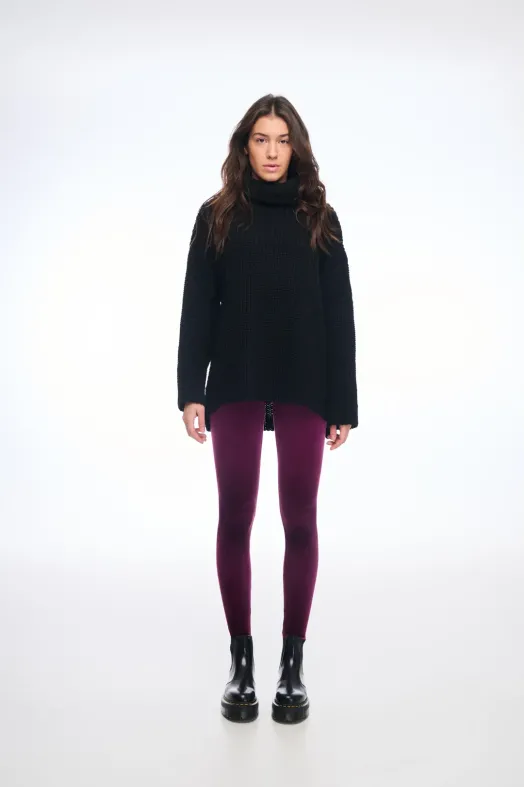 Person wearing a black turtleneck sweater, purple leggings, and black boots on a white background