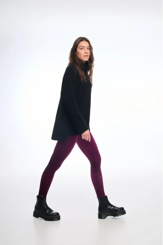 Person wearing a black poncho, purple leggings, and black boots on a white background