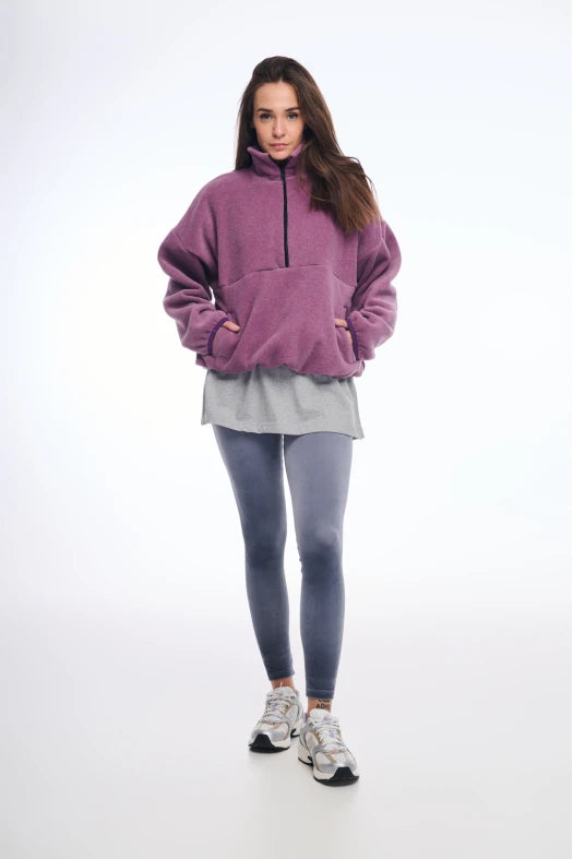Woman wearing a purple fleece pullover, gray shirt, gray leggings, and white sneakers on a white background