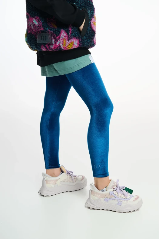 Person wearing blue leggings with a colorful jacket and white sneakers on a light gray background
