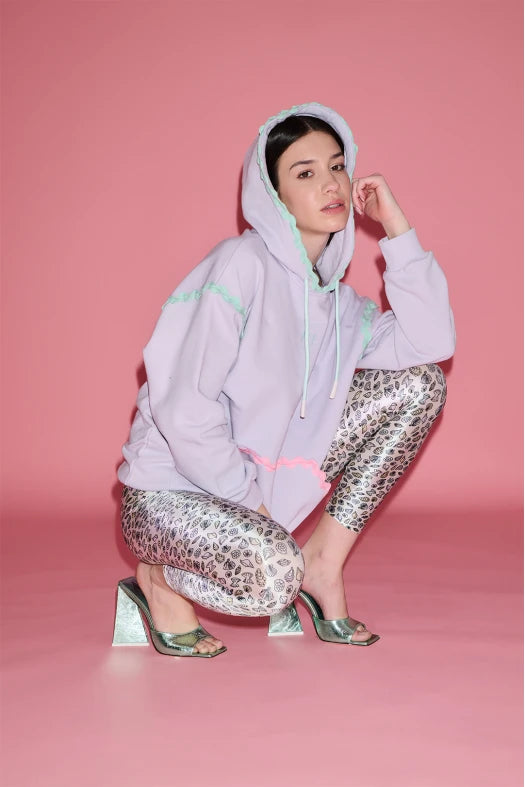 Person wearing a light purple hoodie and patterned pants on a pink background