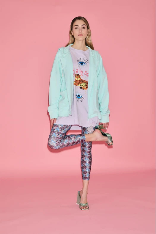 Woman wearing a light blue jacket, pink graphic t-shirt, and patterned leggings on a pink background