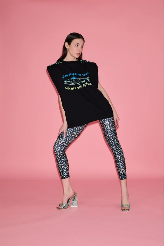 Woman wearing a black sleeveless top with text and graphics, paired with patterned leggings on a pink background