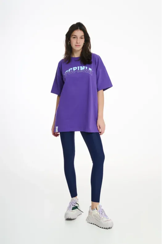 Person wearing a purple oversized t-shirt and dark blue leggings on a white background