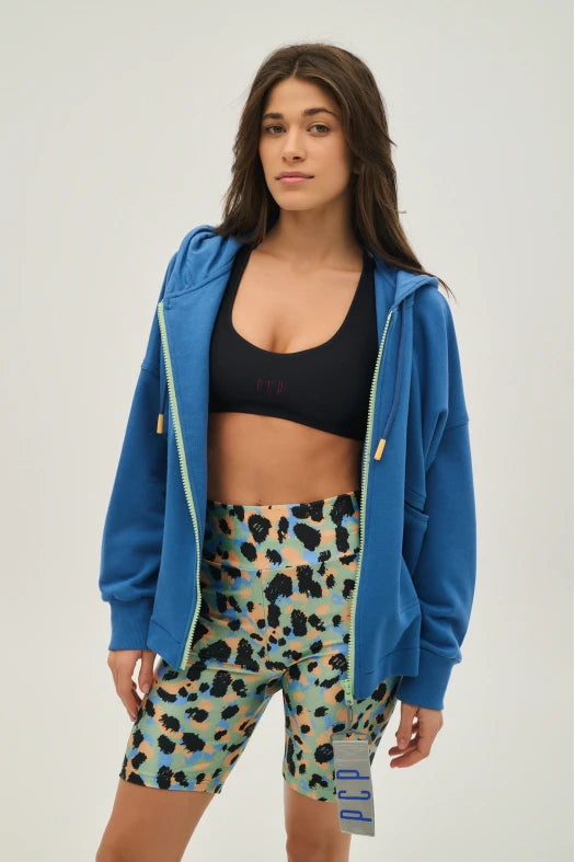 Woman wearing a blue hoodie, black sports bra, and patterned shorts on a light gray background