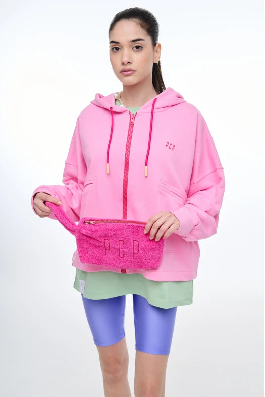 Person wearing a pink hoodie with a visible brand logo, holding a pink pouch with 'PCP' branding.