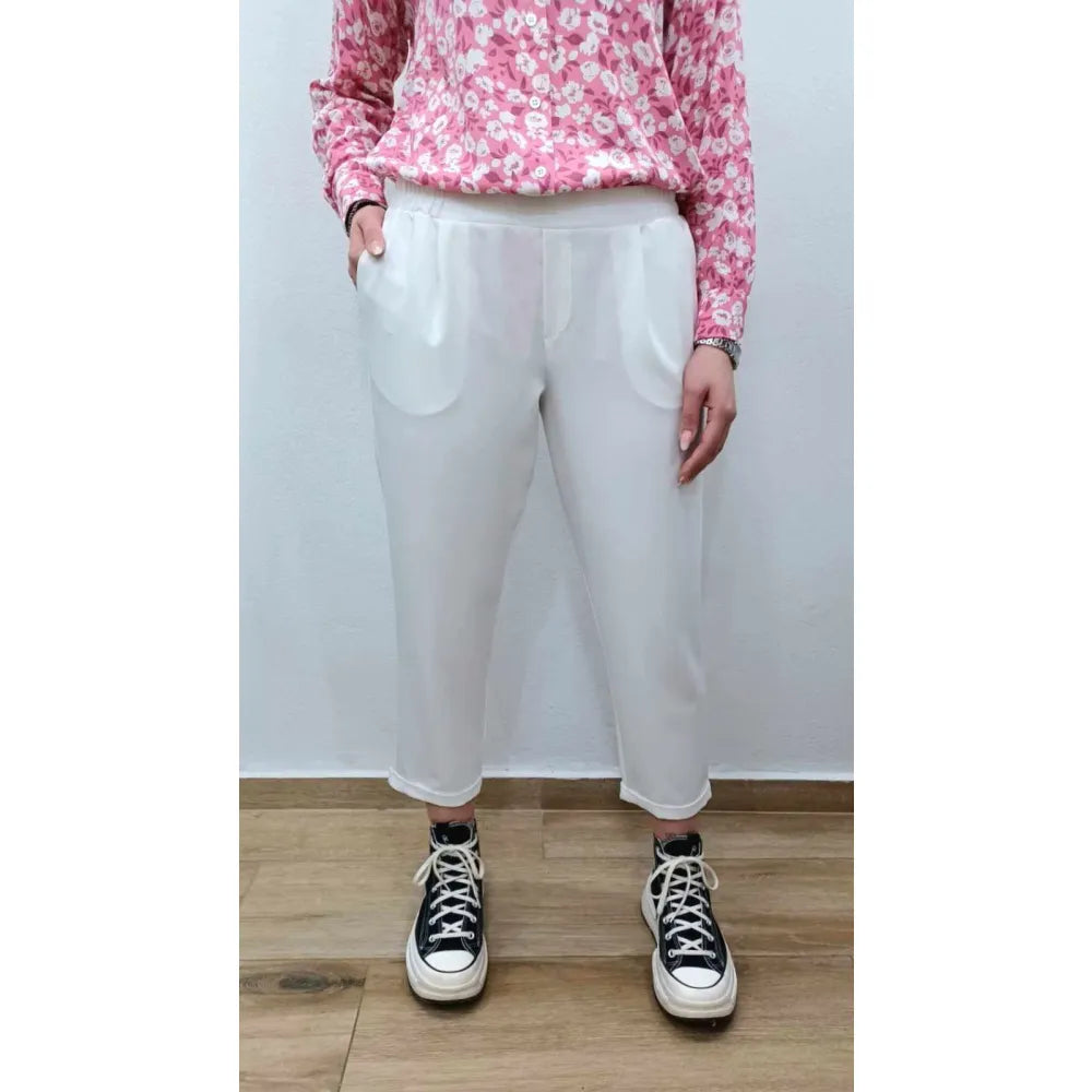 Person wearing a pink floral top, white pants, and black and white sneakers on a plain background