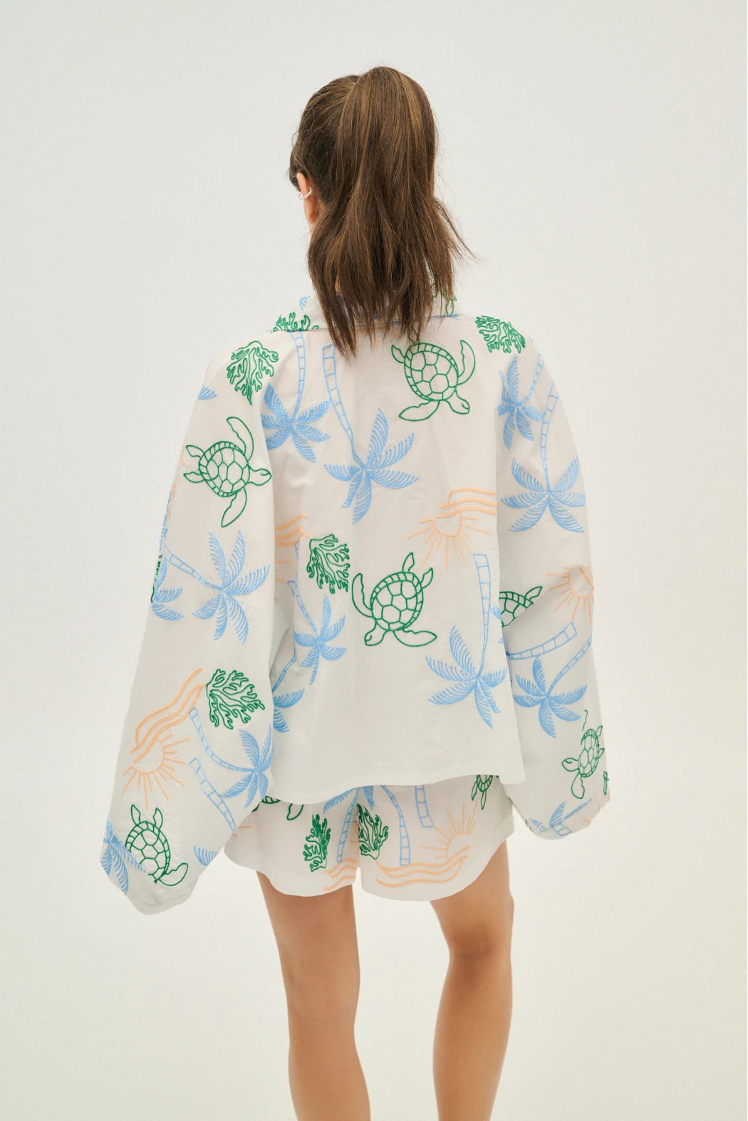 Person wearing a light-colored kimono-style garment with floral and turtle designs on a white background