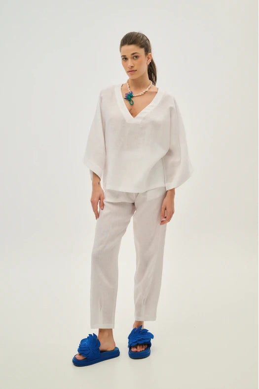 Woman wearing a white outfit with blue sandals on a plain background