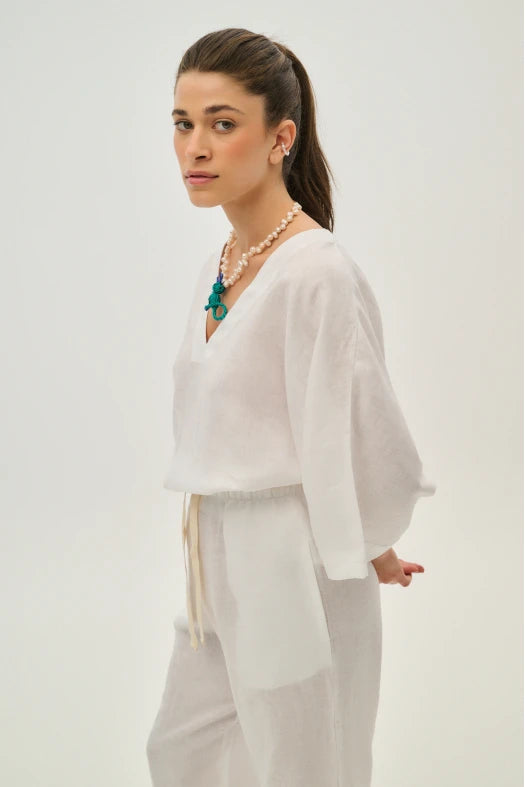 Woman wearing a white outfit with a necklace on a plain background