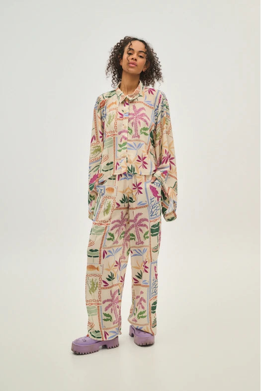 Person wearing a colorful pajama set with floral and palm tree patterns on a white background