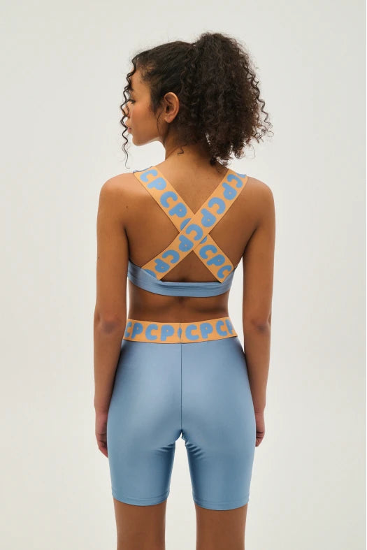 Person wearing a blue sports bra and shorts with a patterned back design on a plain background