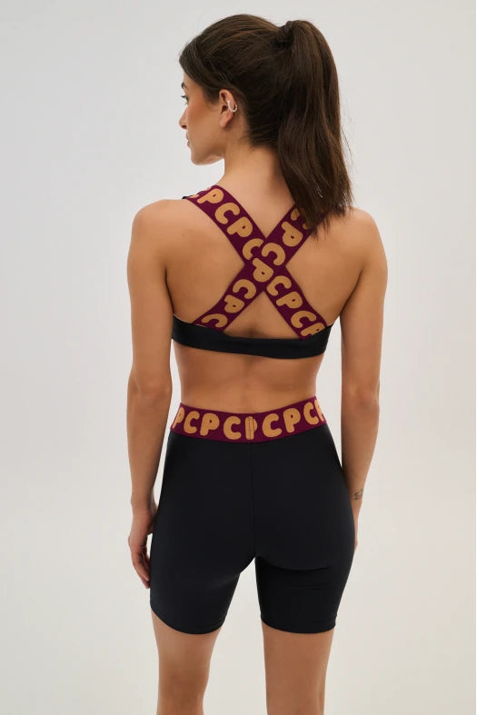 Woman wearing a black sports bra and shorts with red logo straps on a light gray background