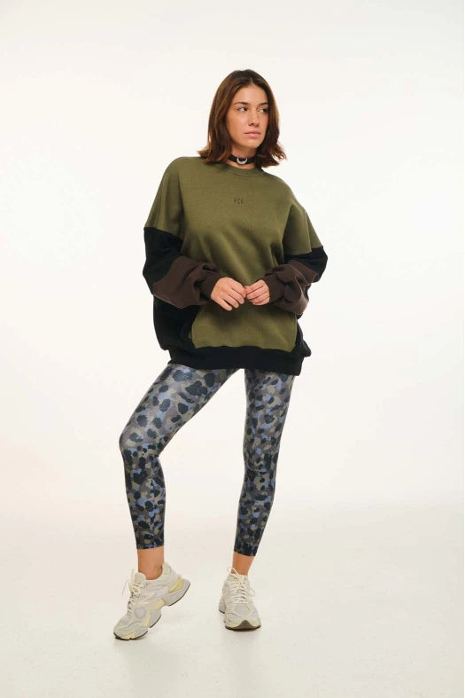 Person wearing a green and black sweater with patterned leggings on a white background
