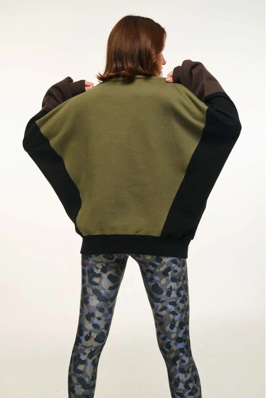 Person wearing a green and black jacket with camouflage pants on a white background