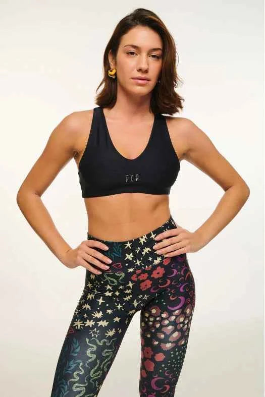 Woman wearing a black sports bra and patterned leggings on a light background