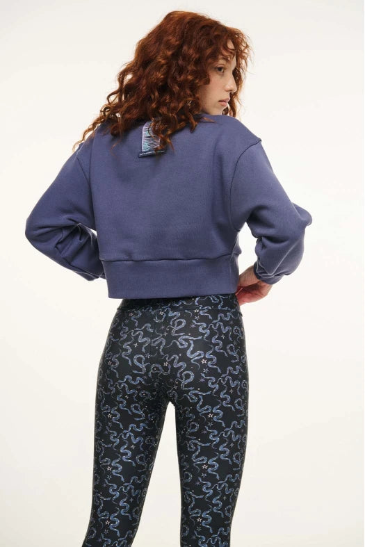 Person wearing a blue sweatshirt and patterned leggings on a white background