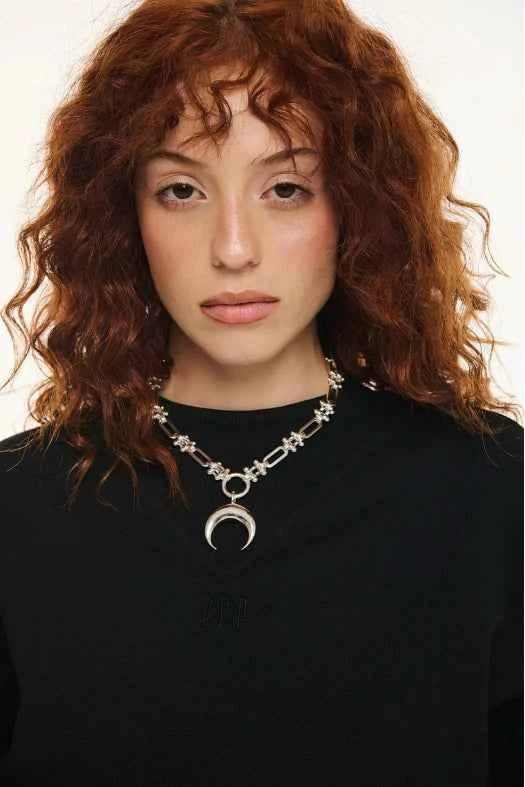 Woman wearing a black top and silver necklace with a crescent moon pendant on a white background