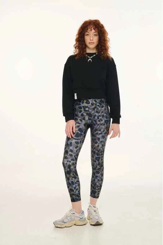 Person wearing a black sweatshirt and patterned leggings on a white background