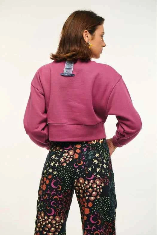 Person wearing a pink sweatshirt and colorful patterned pants on a white background