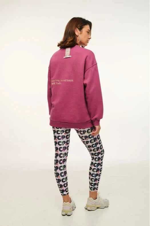 Person wearing a pink sweatshirt and patterned leggings on a white background