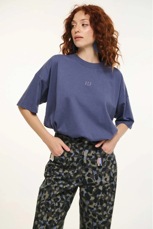 Person wearing a blue oversized shirt and patterned pants on a white background