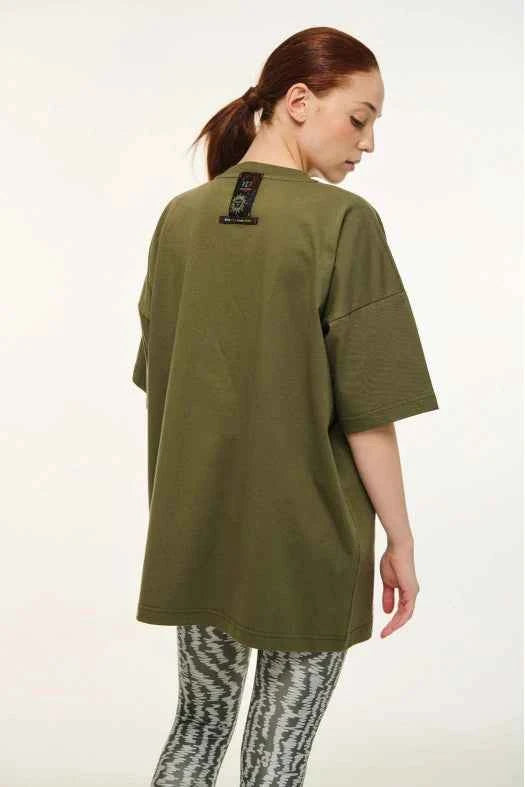 Person wearing a green oversized shirt with a visible brand label on a white background