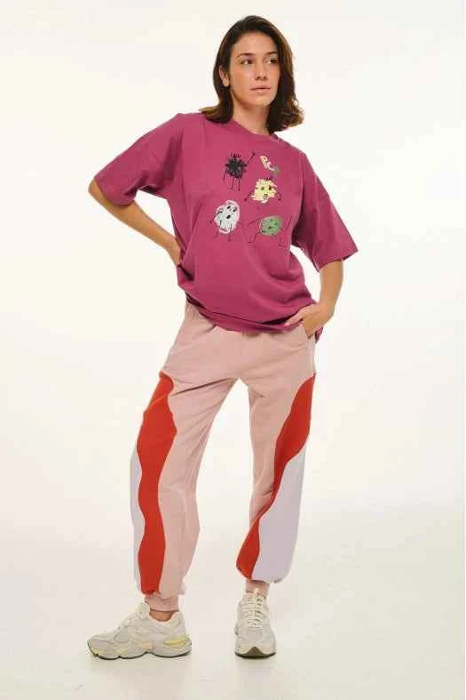 Person wearing a pink oversized t-shirt with floral designs and colorful pants on a white background