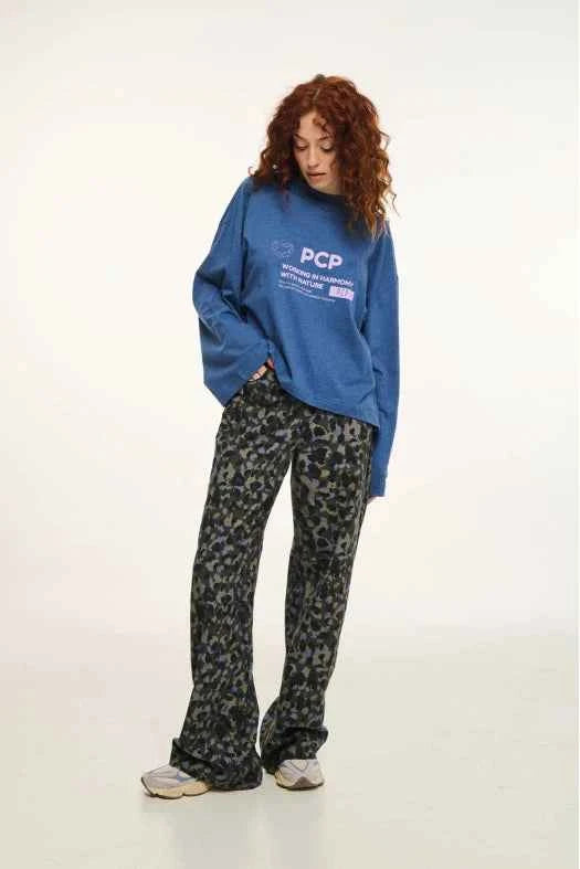 Person wearing a blue sweatshirt with text and patterned pants on a white background