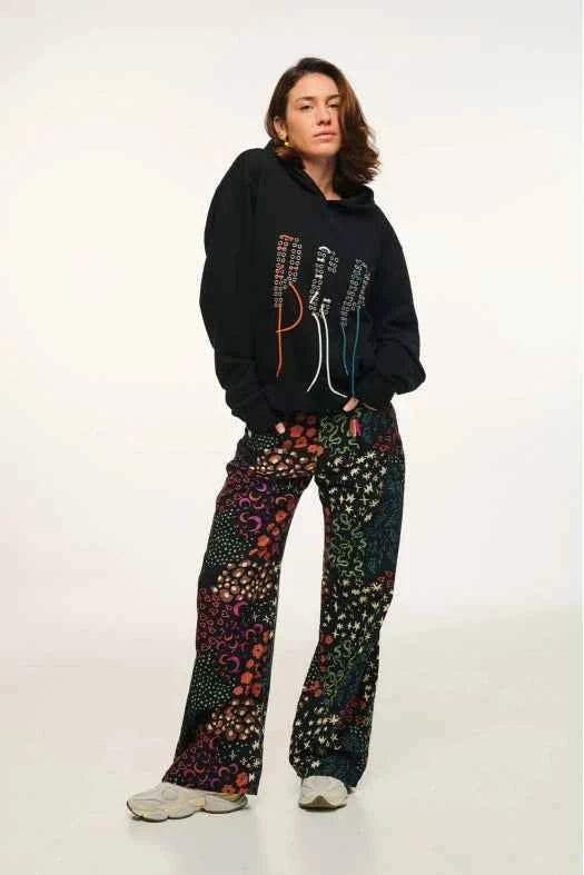 Person wearing a black hoodie with colorful text and patterned pants on a white background