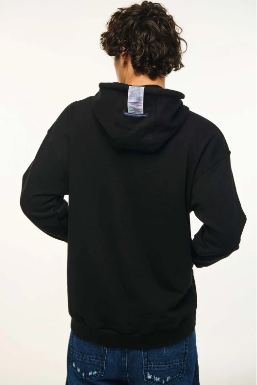 Person wearing a black hoodie with a visible brand label on the back, standing against a white background.