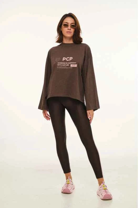 Woman wearing a brown long-sleeve top with a logo and text, black leggings, and pink sneakers on a white background.